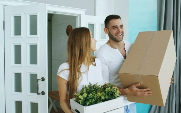 Couple entering their home carrying a cardboard box and indoor plant during move-in