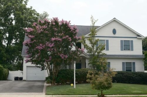 Two-story suburban house with driveway, garage, and trees in a calm residential neighborhood