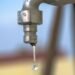 Water dripping from a metal tap showing a slow household leak
