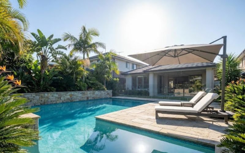 Backyard Pool Costs and Luxury Outdoor Design in 2026 Modern backyard pool with stone patio and tropical landscaping
