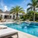Luxury backyard swimming pool with stone patio and tropical landscaping in daylight