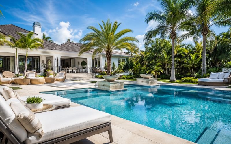Luxury backyard swimming pool with stone patio and tropical landscaping in daylight
