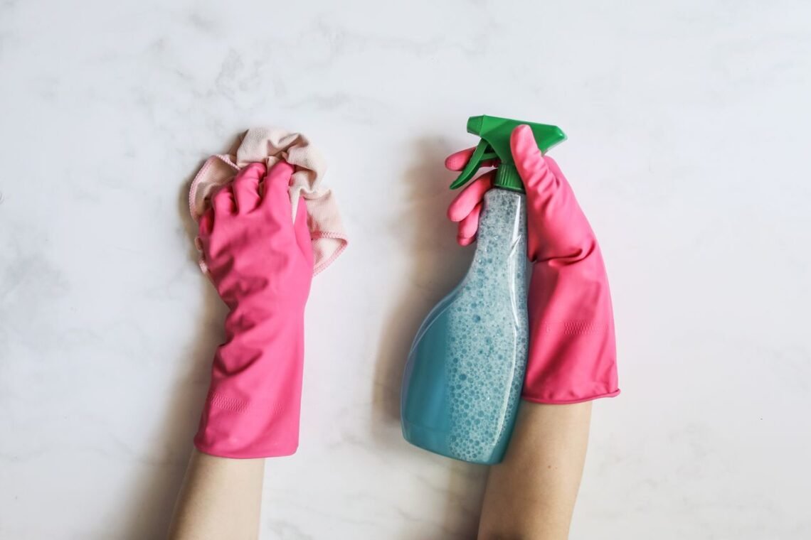 Person wearing pink cleaning gloves wiping a countertop while holding a spray cleaner as part of a healthier home cleaning routine.