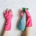 Person wearing pink cleaning gloves wiping a countertop while holding a spray cleaner as part of a healthier home cleaning routine.
