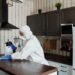 Professional pest control technician performing preventative home maintenance in a modern kitchen